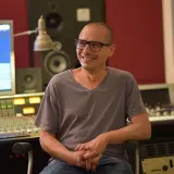 Moses Schneider, lächelnd in einem Tonstudio, sitzt vor einem Mischpult und einem Computerbildschirm.