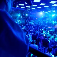 Eine Menge feiert zu den Klängen eines **live DJ** in einem Club. Blaue Lichter tauchen die Szene in eine pulsierende Atmosphäre.
