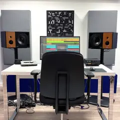 Ein Tonstudio mit Akustikpaneelen in Blau und Grau, die helfen, die **Akustik im Raum verbessern**. Ein Schreibtisch mit Monitor, Lautsprechern und einem Stuhl.