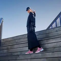 Frau in schwarzem Outfit und Nike Free Rush Schuhen auf Holztreppe.