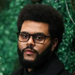 The Weeknd, mit Brille und Bart, posiert vor einer grünen Wand. Seine Musikkarriere begann in Toronto, Kanada.