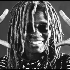 tm stevens mit Dreadlocks und Sonnenbrille, lächelnd und mit beiden Händen die "Rock on"-Geste zeigend.
