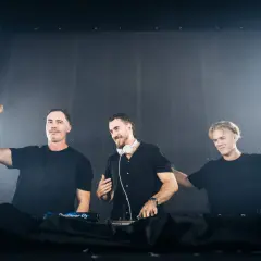 Drei DJs in schwarzen Outfits auf der Bühne, bereit für die Nacht. Aktuelle dj news: Sie rocken die Menge mit ihren Beats.