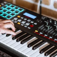 Hand spielt auf einem Keyboard, um Synthesizer-Musik zu kreieren. Bunte Pads und Regler sind sichtbar.