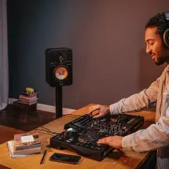 Mann mit Kopfhörern legt Musik auf, um einen DJ-Set aufzunehmen. Zwei Lautsprecher stehen bereit.