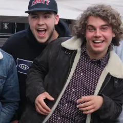 Vier junge Männer, die wie eine rap gruppe aussehen, lachen und posieren vor einer Bühne.