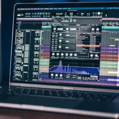 Ein MacBook Pro zeigt eine Musikproduktionssoftware mit einem IR Loader-Plugin, umgeben von Studio-Monitoren.