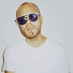 Phil Speiser, mit Sonnenbrille und Zigarette im Mund, trägt ein weißes T-Shirt.