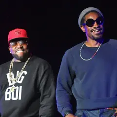 Die Mitglieder von Outkast, Big Boi mit roter Kappe und Andre 3000 mit grauer Mütze, lächeln auf der Bühne.
