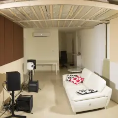 Ein Raum mit weißem Ledersofa, Lautsprechern und einer Deckenkonstruktion, die an ein **Deckensegel selber bauen** Projekt erinnert.
