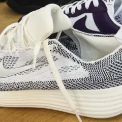 Weiße und schwarze **Shima Shima** Muster zieren diesen Laufschuh. Ein weiterer Schuh in Lila und Weiß ist im Hintergrund zu sehen.