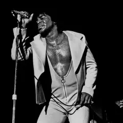 James Brown singt mit geschlossenen Augen und erhobener Hand, ein ikonisches Bild, das an bekannte Funk-Songs erinnert.