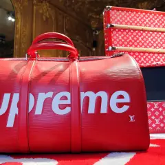 Rote Reisetasche mit weißem "Supreme"-Schriftzug und Louis Vuitton-Monogramm. Was ist Supreme? Luxus und Streetwear vereint.