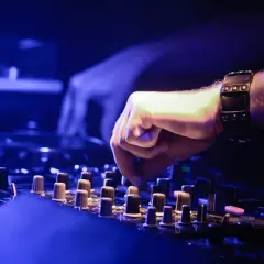 DJ-Hand mit Armband bedient Mischpult, um einen perfekten Mixtape zu erstellen. Blaue Beleuchtung.