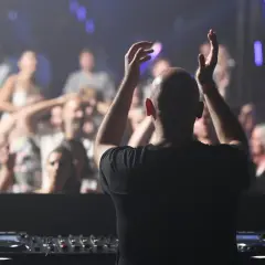 DJ mit erhobenen Armen vor jubelndem Publikum, der algoriddim djay-Controller im Vordergrund.