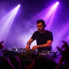 Ein DJ legt im pulsierenden Licht auf, während die Menge jubelt. Der DJ-Pool ist voller Energie und Musik.