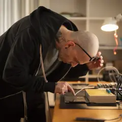 Mann mit Tattoos, der an einem Tisch mit elektronischen Geräten arbeitet, inspiriert von russischem Konstruktivismus.