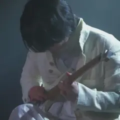 Ein Musiker in weißer Kleidung spielt eine Gitarre. Die Szene ist düster beleuchtet, was die Konzentration auf die Performance von Ichika Nito verstärkt.