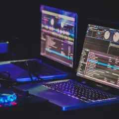 Zwei Laptops mit DJ-Software, beleuchtet von blauem und pinkem Licht, bereit für den nächsten Beat.