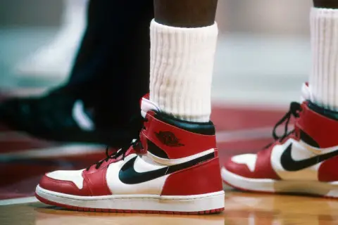 Ein Paar ikonische Air Jordan 1 Sneaker in Rot und Weiß, vielleicht der teuerste Schuh der Welt, auf einem Basketballplatz.