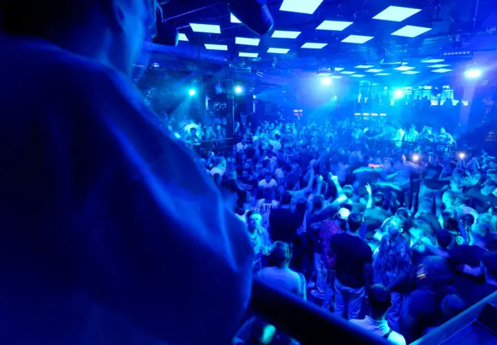 Eine Menge feiert zu den Klängen eines **live DJ** in einem Club. Blaue Lichter tauchen die Szene in eine pulsierende Atmosphäre.
