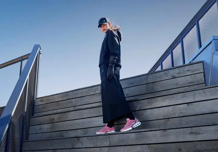 Frau in schwarzem Outfit und Nike Free Rush Schuhen auf Holztreppe.