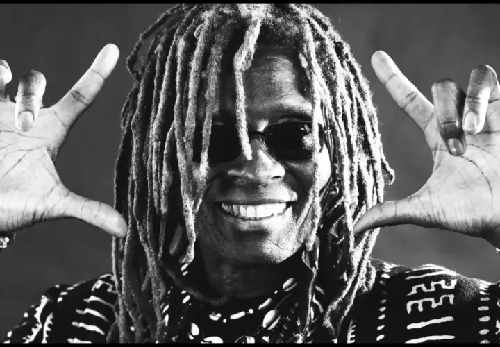 tm stevens mit Dreadlocks und Sonnenbrille, lächelnd und mit beiden Händen die "Rock on"-Geste zeigend.