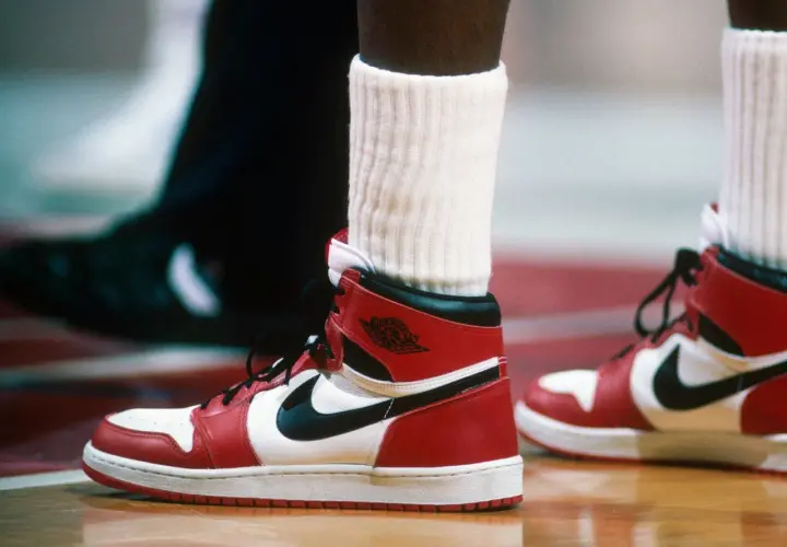 Ein Paar ikonische Air Jordan 1 Sneaker in Rot und Weiß, vielleicht der teuerste Schuh der Welt, auf einem Basketballplatz.