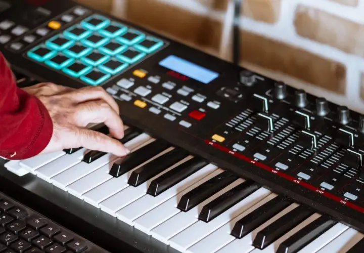 Hand spielt auf einem Keyboard, um Synthesizer-Musik zu kreieren. Bunte Pads und Regler sind sichtbar.