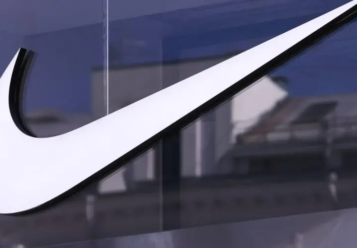 Das ikonische Nike-Logo, ein Symbol für die Nike Logo Entwicklung, leuchtet weiß vor einem blauen Himmel und reflektiert Gebäude.