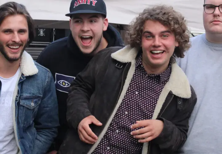 Vier junge Männer, die wie eine rap gruppe aussehen, lachen und posieren vor einer Bühne.