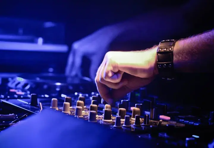 DJ-Hand mit Armband bedient Mischpult, um einen perfekten Mixtape zu erstellen. Blaue Beleuchtung.