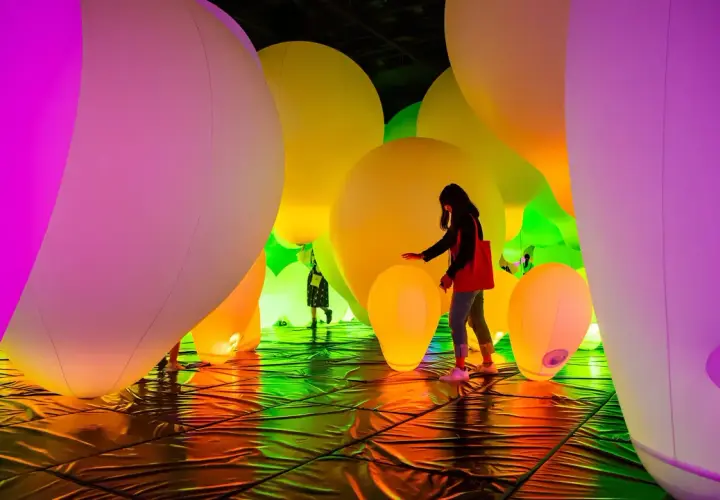 Menschen interagieren mit einer leuchtenden Installation aus riesigen, bunten Ballons. Ein immersives Kunsterlebnis.