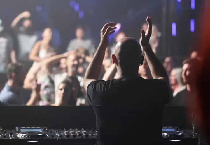 DJ mit erhobenen Armen vor jubelndem Publikum, der algoriddim djay-Controller im Vordergrund.
