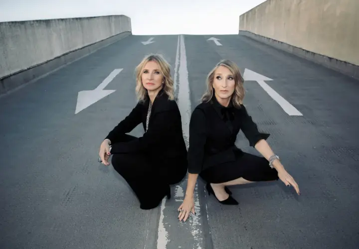 Susanne Freytag und ihre Partnerin, beide in eleganten schwarzen Outfits, hocken auf einer asphaltierten Rampe mit weißen Pfeilen.