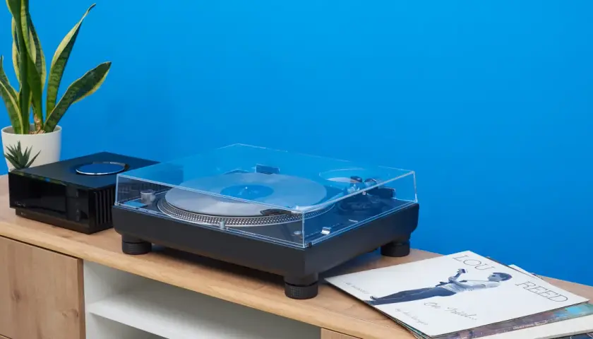 Technics SL-1210GR Plattenspieler mit Vinyl und Pflanzen auf einem Sideboard vor blauer Wand.