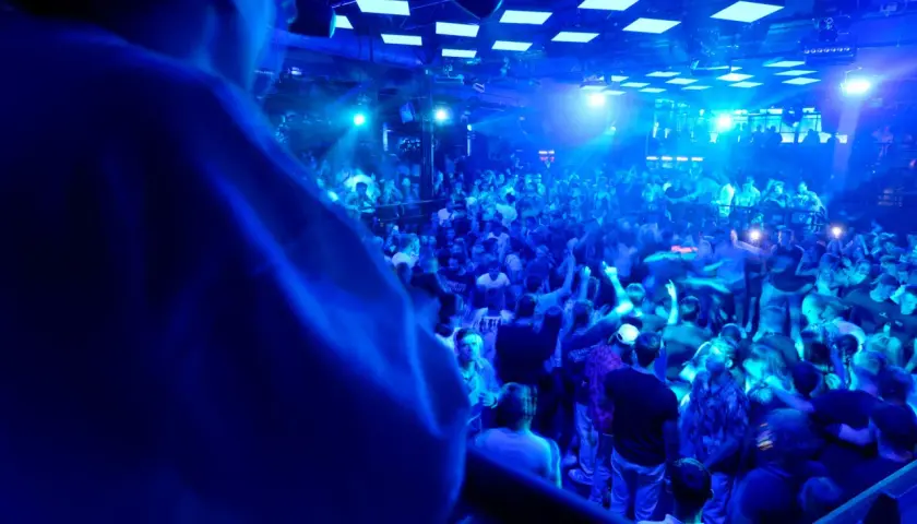 Eine Menge feiert zu den Klängen eines **live DJ** in einem Club. Blaue Lichter tauchen die Szene in eine pulsierende Atmosphäre.