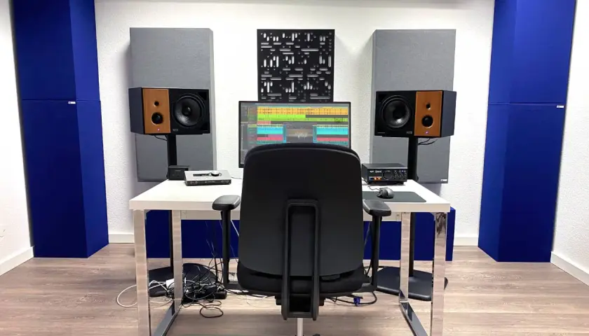 Ein Tonstudio mit Akustikpaneelen in Blau und Grau, die helfen, die **Akustik im Raum verbessern**. Ein Schreibtisch mit Monitor, Lautsprechern und einem Stuhl.