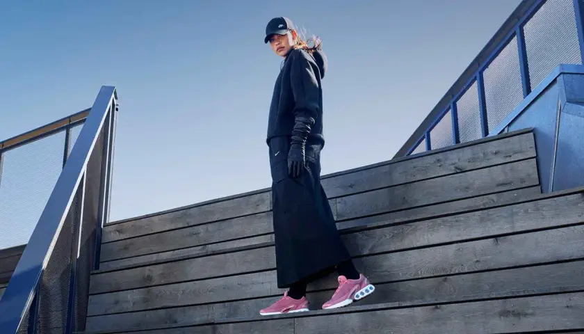 Frau in schwarzem Outfit und Nike Free Rush Schuhen auf Holztreppe.