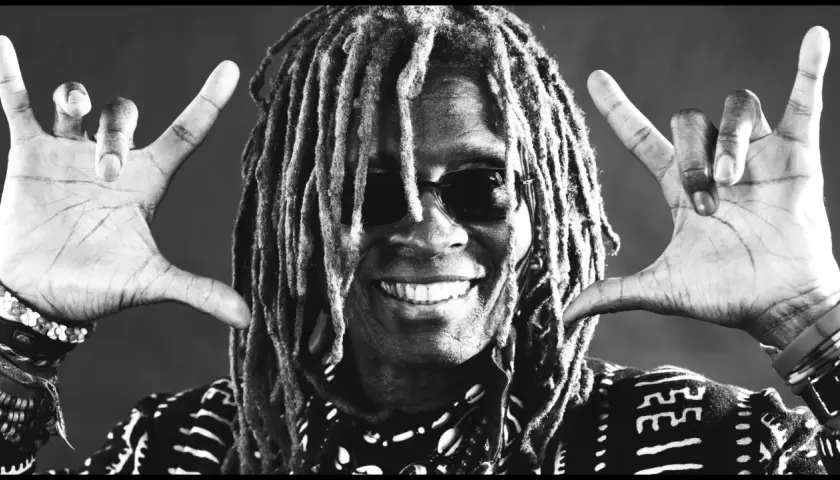 tm stevens mit Dreadlocks und Sonnenbrille, lächelnd und mit beiden Händen die "Rock on"-Geste zeigend.
