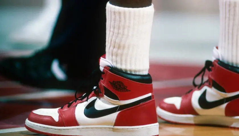 Ein Paar ikonische Air Jordan 1 Sneaker in Rot und Weiß, vielleicht der teuerste Schuh der Welt, auf einem Basketballplatz.