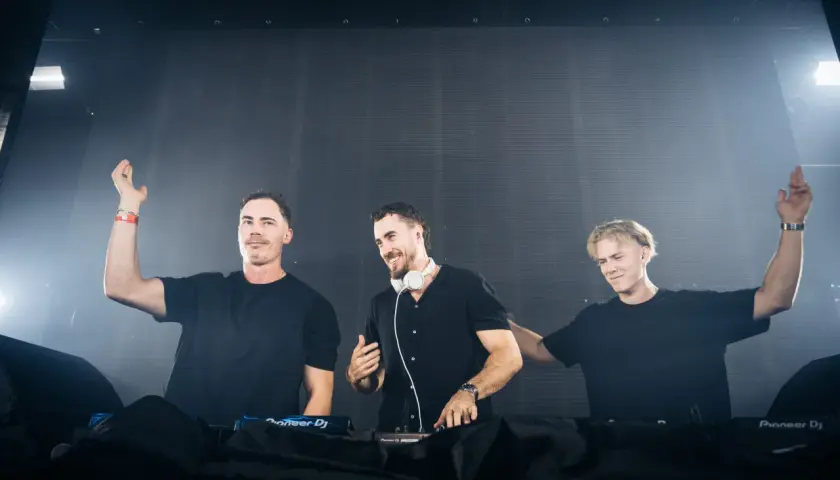 Drei DJs in schwarzen Outfits auf der Bühne, bereit für die Nacht. Aktuelle dj news: Sie rocken die Menge mit ihren Beats.