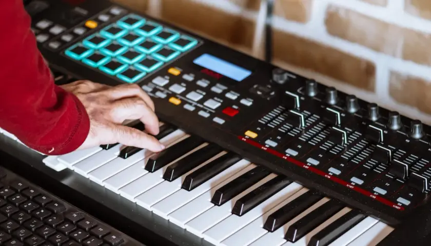 Hand spielt auf einem Keyboard, um Synthesizer-Musik zu kreieren. Bunte Pads und Regler sind sichtbar.