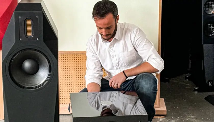 Mann im weißen Hemd und Jeans macht einen **subwoofer test** vor einem großen schwarzen Lautsprecher.