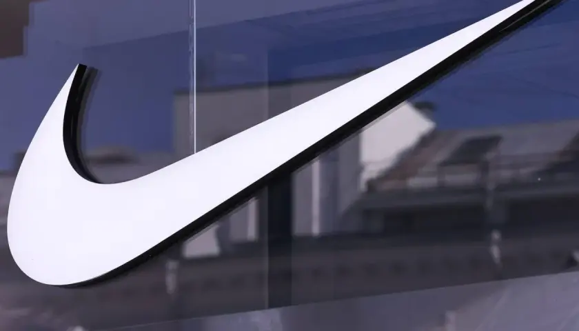 Das ikonische Nike-Logo, ein Symbol für die Nike Logo Entwicklung, leuchtet weiß vor einem blauen Himmel und reflektiert Gebäude.