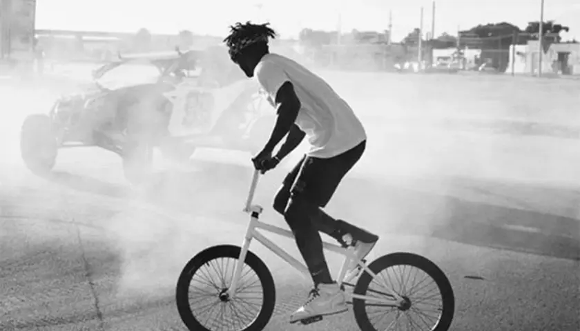 Nigel Sylvester fährt BMX, während im Hintergrund ein Buggy im Rauch steht.