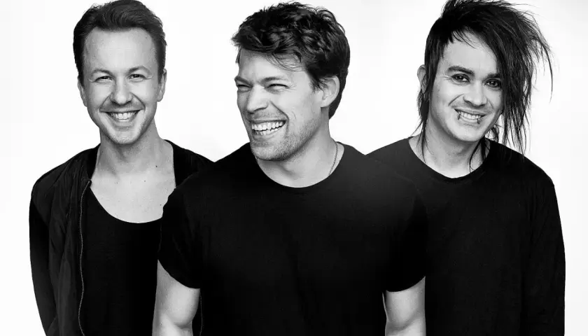 Drei Männer in schwarzen T-Shirts lachen. Der mittlere Mann, Henrik Linder, lacht am lautesten.