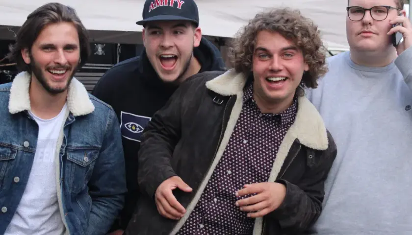 Vier junge Männer, die wie eine rap gruppe aussehen, lachen und posieren vor einer Bühne.