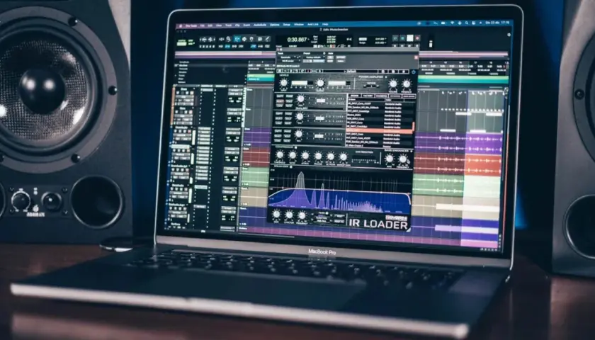 Ein MacBook Pro zeigt eine Musikproduktionssoftware mit einem IR Loader-Plugin, umgeben von Studio-Monitoren.