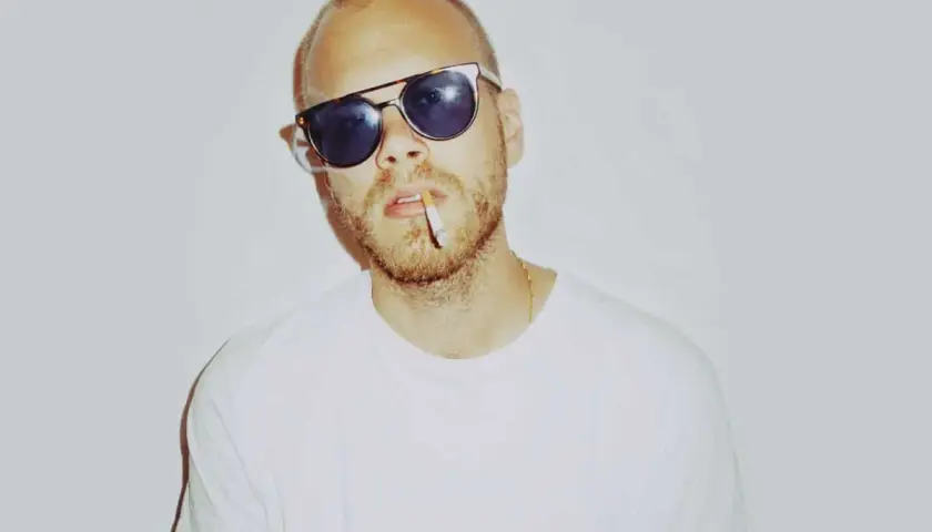 Phil Speiser, mit Sonnenbrille und Zigarette im Mund, trägt ein weißes T-Shirt.